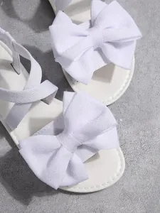 Detailansicht weißer eleganter Sandalen mit übergroßen dekorativen Stoffschleifen und Textur