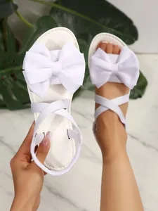 Detailansicht weißer Sandalen mit einer großen Schleife und eleganten Überkreuzriemen