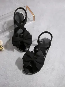 Detail von schwarzen Schleifensandalen mit elastischen Kreuzgurten und flacher Sohle