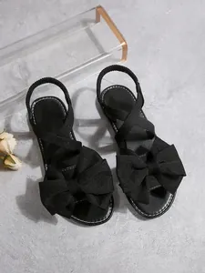 Detailansicht schwarzer flacher Sandalen mit großer Schleife und elastischen Riemen