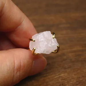 Close-up of raw rose quartz ring with gold claw setting on a warm wooden background