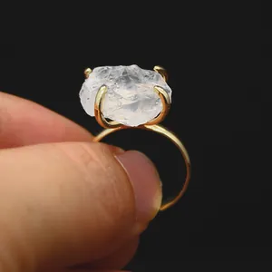 Close-up of raw white crystal ring with golden claw setting on adjustable band