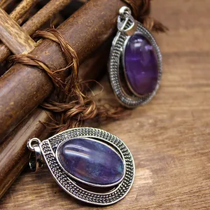 Detailed view of two vintage teardrop pendants featuring purple oval crystals on rustic wood.