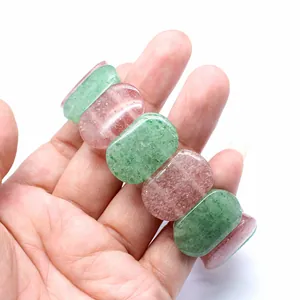Close-up view of a natural strawberry quartz and green stone bracelet held on a hand.