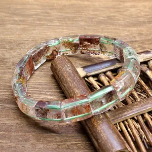 Detailed macro view of natural green phantom and red jiao hua crystal slab bracelet on wood
