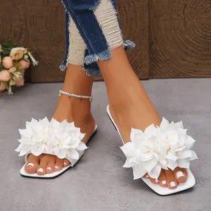 Detailed view of white flat slide sandals featuring elegant 3D fabric flower decorations.