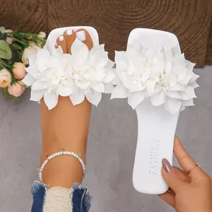 Close-up view of white flat sandals featuring large decorative 3D fabric flowers