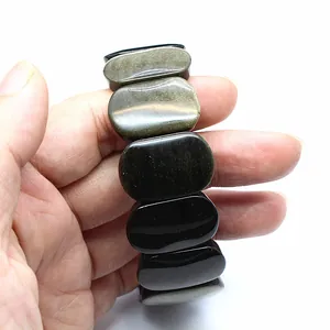 Close-up detail view of smooth oval golden obsidian natural stone bracelet held in hand.