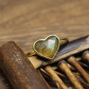 Macro detail of a heart-shaped faceted labradorite ring in a gold setting on a rustic wood background