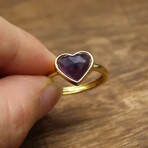 Detail view of a gold open ring featuring a faceted purple heart-shaped crystal stone