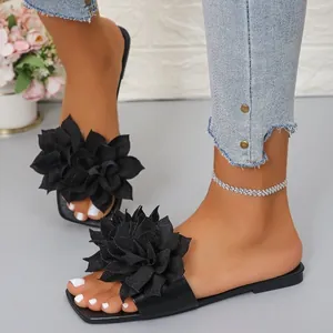 Close-up view of elegant black flat sandals featuring a large decorative 3D flower ornament