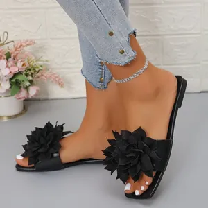 Detailed view of black flat sandals featuring a large fabric flower accent for women.