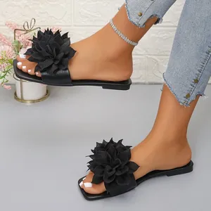Close-up of elegant black flat slide sandals featuring an oversized fabric flower detail