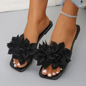 Close-up view of black flat sandals featuring large stylish 3D fabric flower decorations