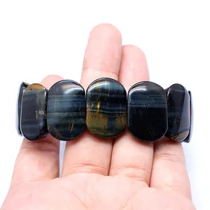 Close-up of smooth oval blue tiger eye stone bracelet held on hand for detail view.