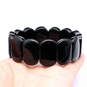 Close-up view of polished black oval stone bracelet beads held in a person's hand