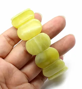 Detailed close-up of a natural yellow-green oval gemstone hand-row bracelet held in hand.