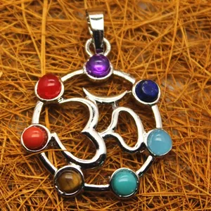 Detailed view of silver Om pendant with seven chakra gemstones on straw background