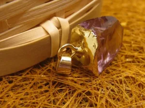 Détail d'un pendentif en améthyste brute violette avec une bélière plaquée or 24k.
