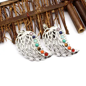 Close-up of two silver wing-shaped pendants featuring seven colorful chakra gemstones.