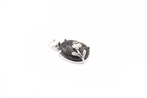 Detailed macro view of a natural black lava stone pendant with silver rose motif