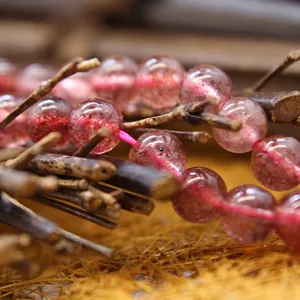 Natural pink strawberry quartz crystal round beads displayed on rustic wooden branches for DIY