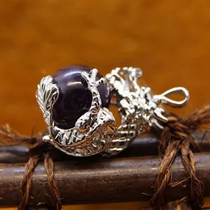 Intricate silver dragon pendant clutching a purple volcanic stone bead on rustic background