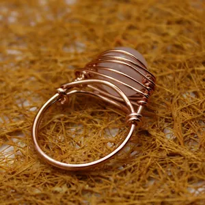 Anillo artesanal de alambre de oro rosa con ágata rosa sobre fondo de paja natural
