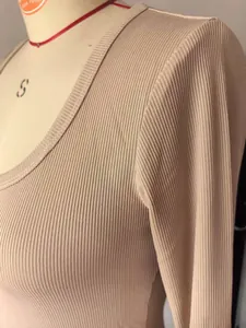 Detail van de fijne geribbelde gebreide textuur van een beige top met lange mouwen en vierkante hals