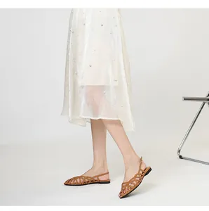 Macro view of brown woven Roman flat sandals worn with an elegant white pearl skirt