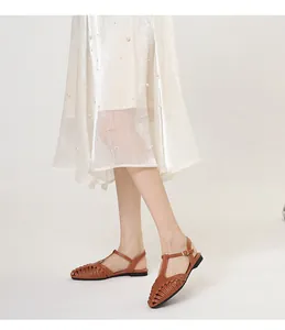 Detail of French retro brown woven T-strap flat sandals with a pearled skirt background