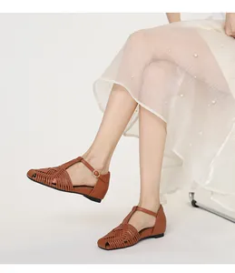 Detailed view of brown woven T-strap sandals worn with a white pearl skirt