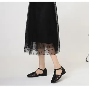 Detail view of black woven T-strap sandals worn by model with black mesh skirt.