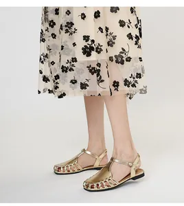 Close-up of metallic gold caged Roman sandals worn with a floral skirt.