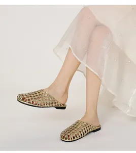 Primer plano elegante de mules planos trenzados dorados usados por una modelo en verano.