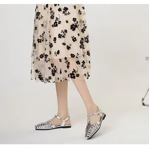 Close-up of silver French retro T-strap woven flat sandals worn with floral skirt.