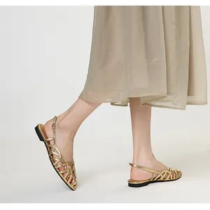 Close-up detail of golden woven straps on elegant flat sandals worn by a model in a skirt.