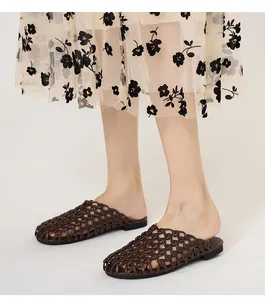 Detalle de cerca de sandalias planas tipo mule tejidas en marrón oscuro con falda floral.