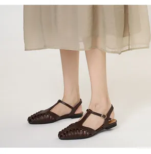 Detailed view of dark brown woven T-strap flat sandals paired with a flowing light dress