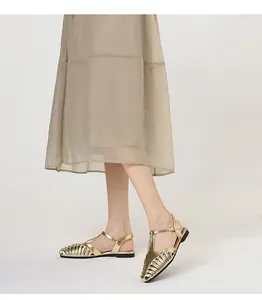 Detail shot of metallic gold T-strap woven Roman sandals worn with a beige skirt.