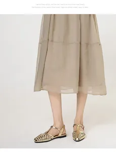 Close-up detail of stylish gold woven T-strap flat sandals worn with a beige skirt.