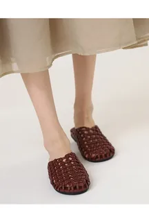 Primer plano de mules retro de cuero trenzado con diseño calado en los pies de la modelo
