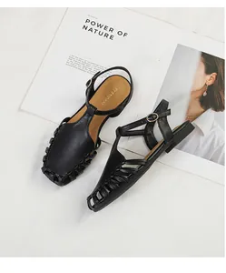 Close-up of black hollow closed-toe Roman sandals with a buckle strap on a white background.