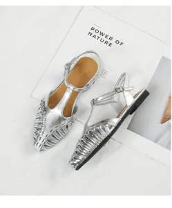 Detail of silver T-strap sandals with intricate hollow woven texture and pointed toe.