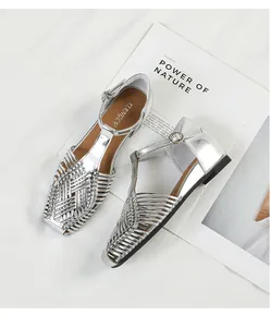 Detailed view of silver metallic woven T-strap sandals with square toe on white prop