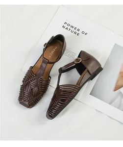 Detail of brown woven T-strap sandals with square toe and gold buckle closure.