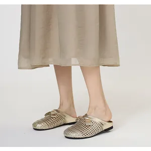 Elegante goldene geflochtene Pantoletten mit Schleife, getragen von einem Modell.