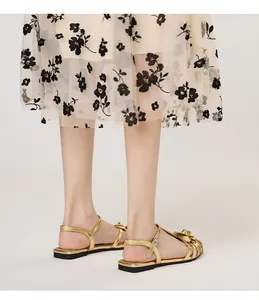Detailed view of gold camellia flower flat sandals with adjustable ankle straps.