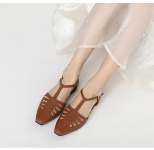 Close-up view of vintage brown hollow-out flat sandals with T-strap worn by model