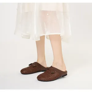 Detailansicht der stylischen braunen geflochtenen Pantoletten mit Schleife am Model.